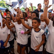 Crianças estudantes da Comunidade do Aço juntas com as mãos para cima participando de atividades lúdicas